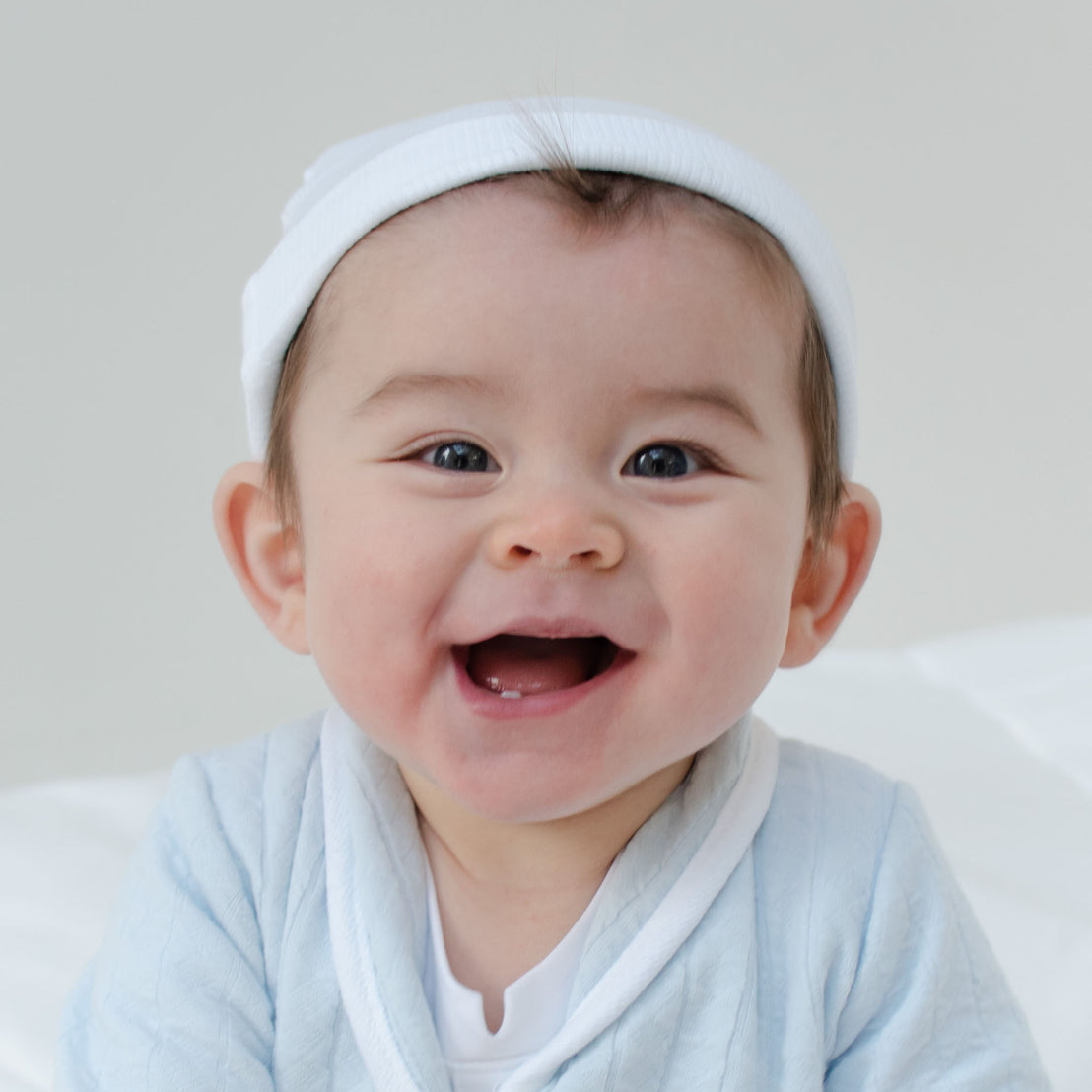 Smiling baby boy wearing the White Ribbed Cotton Beanie made from 100% ribbed textured cotton.
