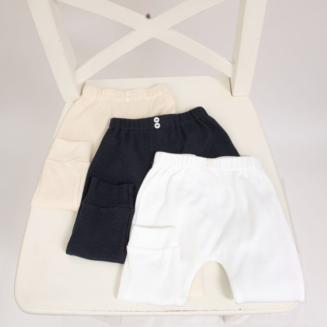 Flat lay photo of three ribbed cotton leggings (with button detail) in different colors, including ivory, navy, and white.