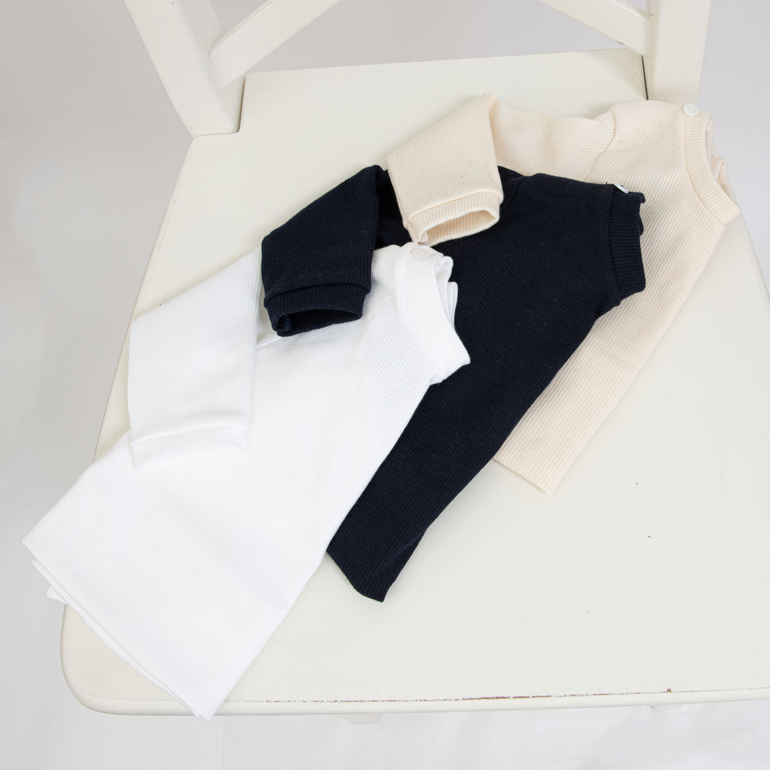 Flat lay photo of three ribbed cotton tops (with button detail) in different colors, including ivory, navy, and white.