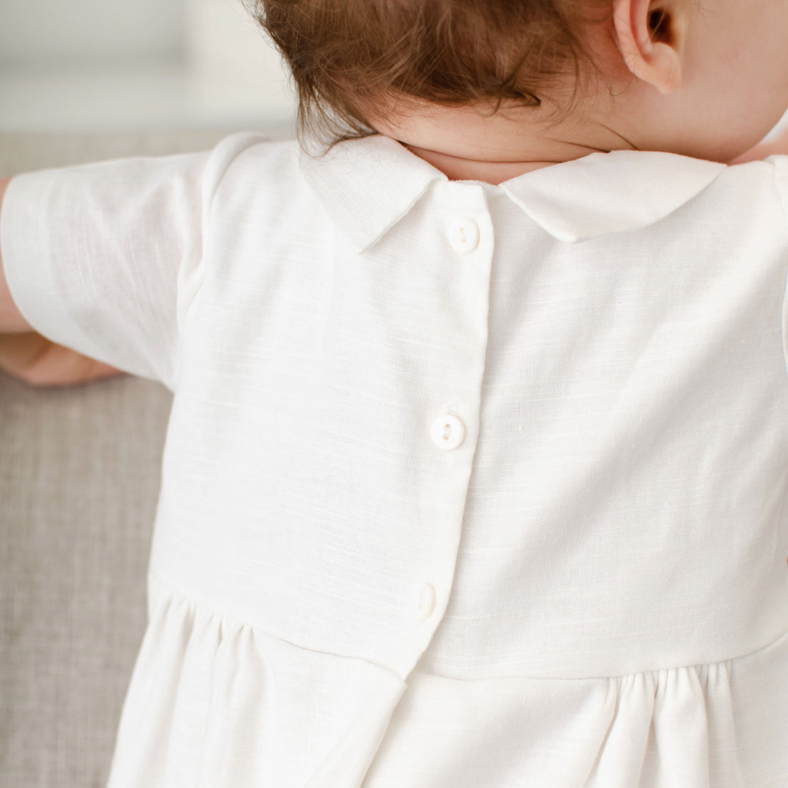 Closer detail of the back of a baby boy wearing the Oliver Bubble Romper. The back of the romper features a 3-button back bodice closure.