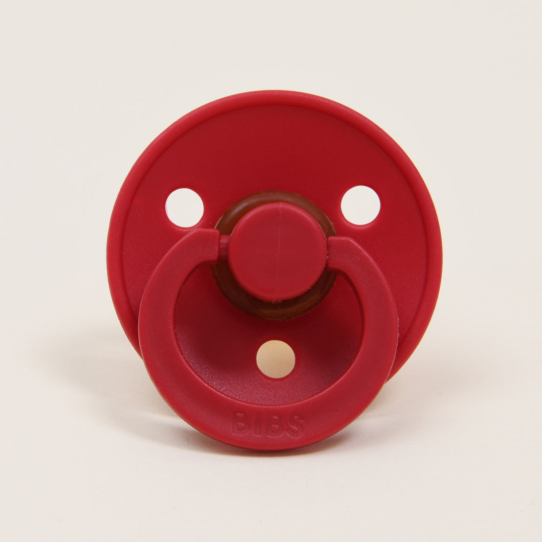 A Bibs Pacifier in Ruby with a button handle, displayed against a plain white background, perfect as an upscale baby gift.