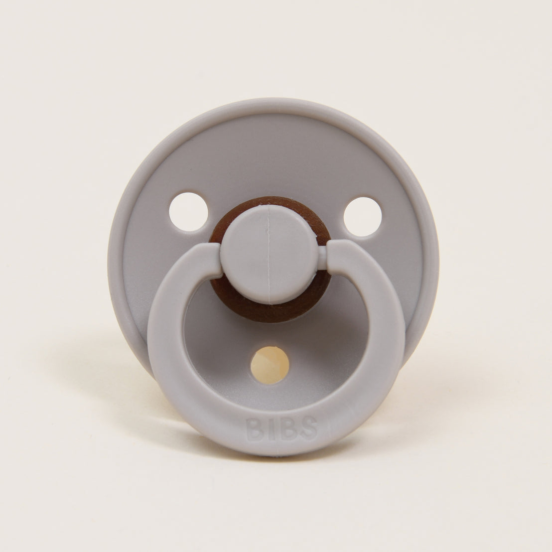 A Bibs Pacifier in Sand featuring an upscale design with two air holes and a natural brown button handle, set against a plain white background. Perfect as a baby gift.