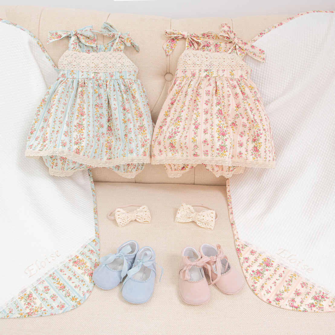 Flat lay photo of the complete Eloise outfit and collection, including the Eloise Romper Dress, Eloise Bow Headband, Eloise Suede Tie Mary Janes, and Eloise Personalized Blanket in the two color variations "sky blue" and "blush".