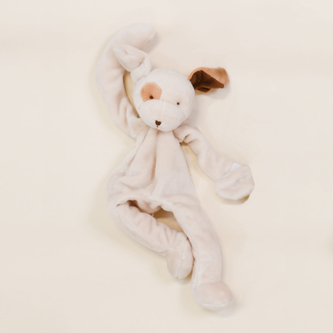 A soft, plush toy rabbit with floppy ears, one ear brown and the other white, on a light beige background. The Baby Beau & Belle Silly Puppy Buddy pacifier holder is lying flat, facing upwards.