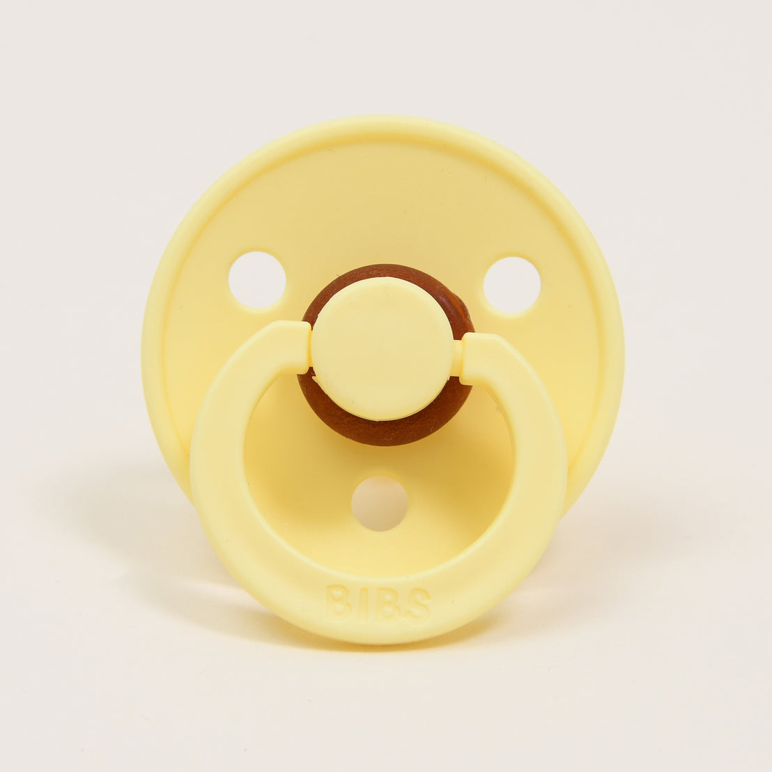 A yellow Bibs Pacifier in Sunshine color with a brown button detail, branded "bibs".