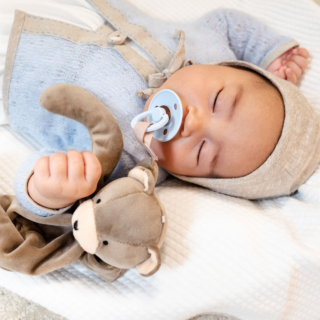 A peaceful baby with an Austin Bear Buddy Pacifier Holder sleeps soundly while snuggling.