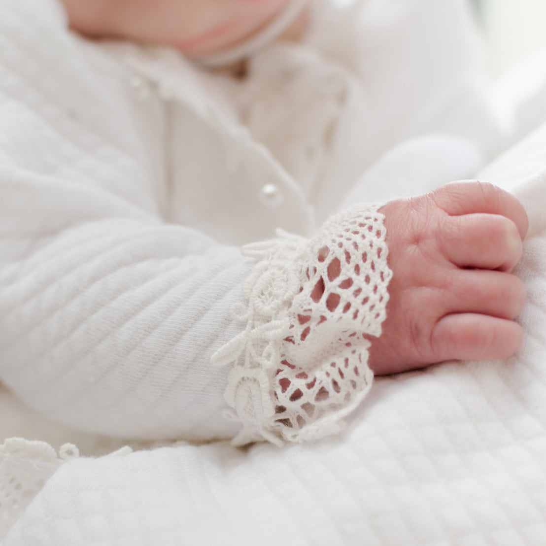 Baby's sleeve of the Lily Quilted Cotton Sweater showing the detail of the ivory cotton lace with rose and vine floral embroidery 