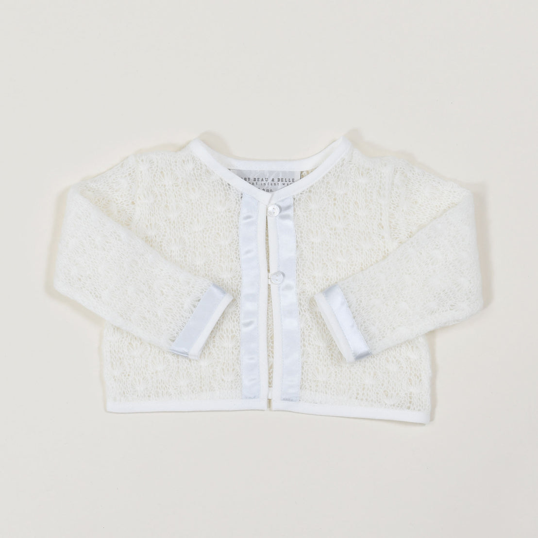 Flat lay photo of the Owen Knit Sweater made from a soft knit in ivory and trimmed with ivory linen and blue silk ribbon