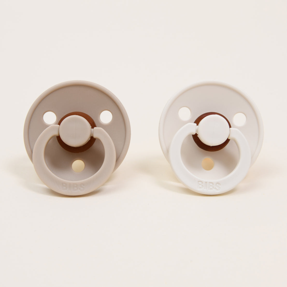 One vanilla and one ivory Bibs Pacifiers with the brand name bibs inscribed.