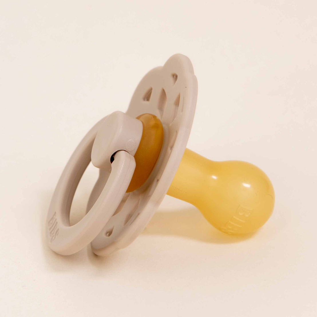 The Chloe Pacifier Set in Ivory & Vanilla, crafted in Denmark with natural rubber, includes a ring and an ergonomic nipple, displayed against a neutral background. It's expertly designed to help little ones self-soothe effortlessly.