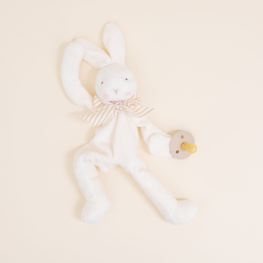 Flat lay photo of the tan Theodore Bunny Buddy Pacifier Holder. Stuffed animal floppy bunny made from a soft velour.