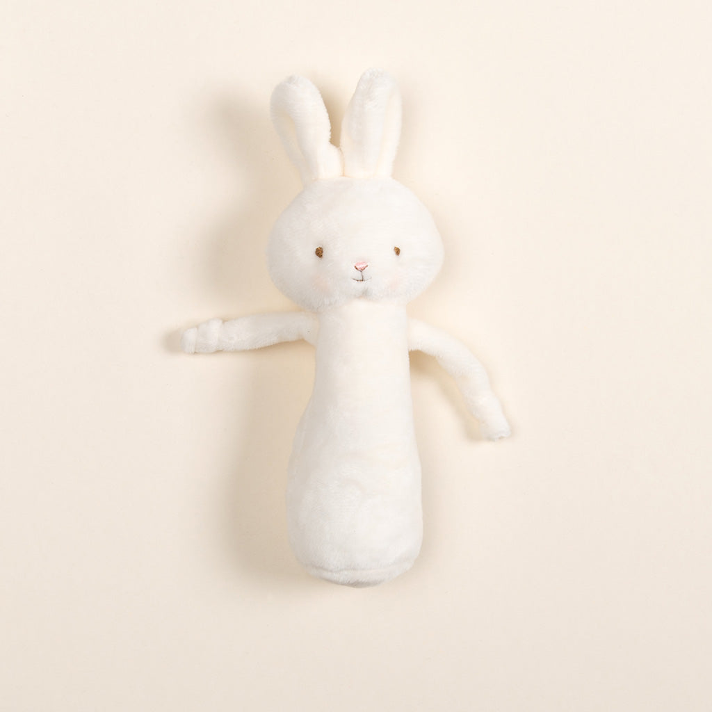 A soft, plush toy designed as a white bunny with floppy ears and stitched eyes and mouth rests against a plain, light cream background. The Plush Chime Rattle is baby-safe with a gentle chime inside and is wrapped in delicate baby blue velour for an added touch of charm.
