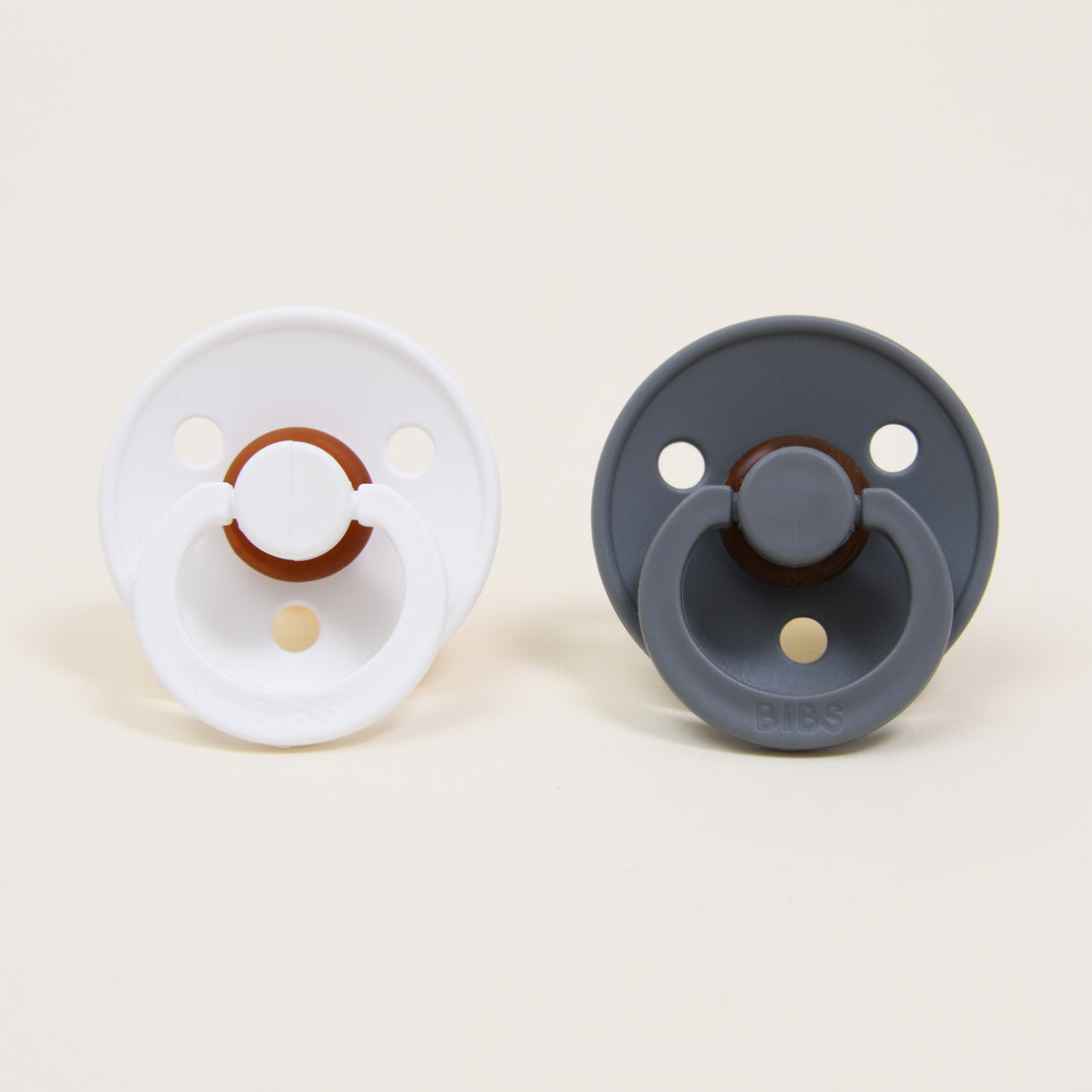 Two Bibs Pacifiers in white and smoke, viewed from the front against a plain beige background, perfect as a natural baby gift.