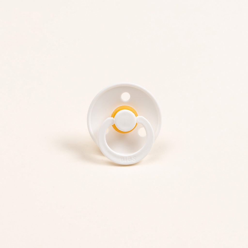 The Silly Bunny Buddy & Pacifier, featuring a sleek white design with a small yellow ring and smooth, round base, sits elegantly against the plain off-white background, making it an ideal baby gift.