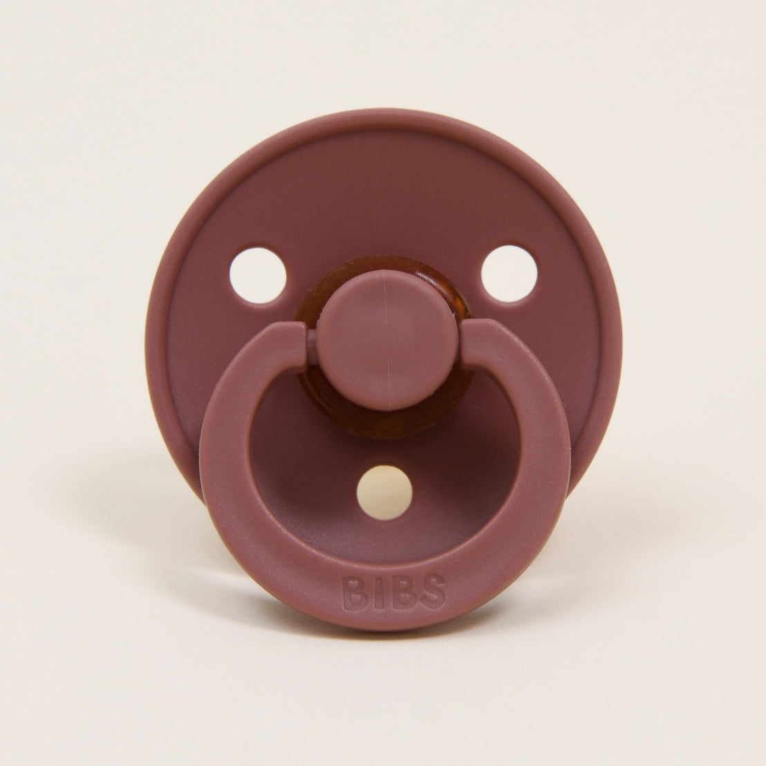A maroon-colored Bibs Pacifier with three air holes, featuring a handle and "bibs" brand name on the button.