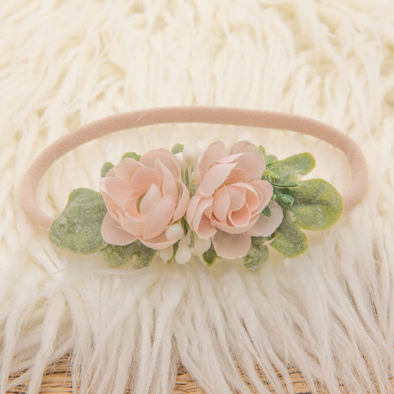 The Ava Petite Flower Headband, adorned with blush pink roses and green leaves, is elegantly showcased on a soft white background.