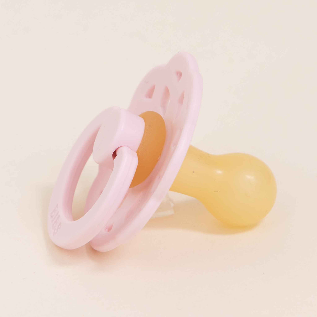 A pink and yellow Bibs Lace Pacifier made from natural rubber, lying on a light beige background.