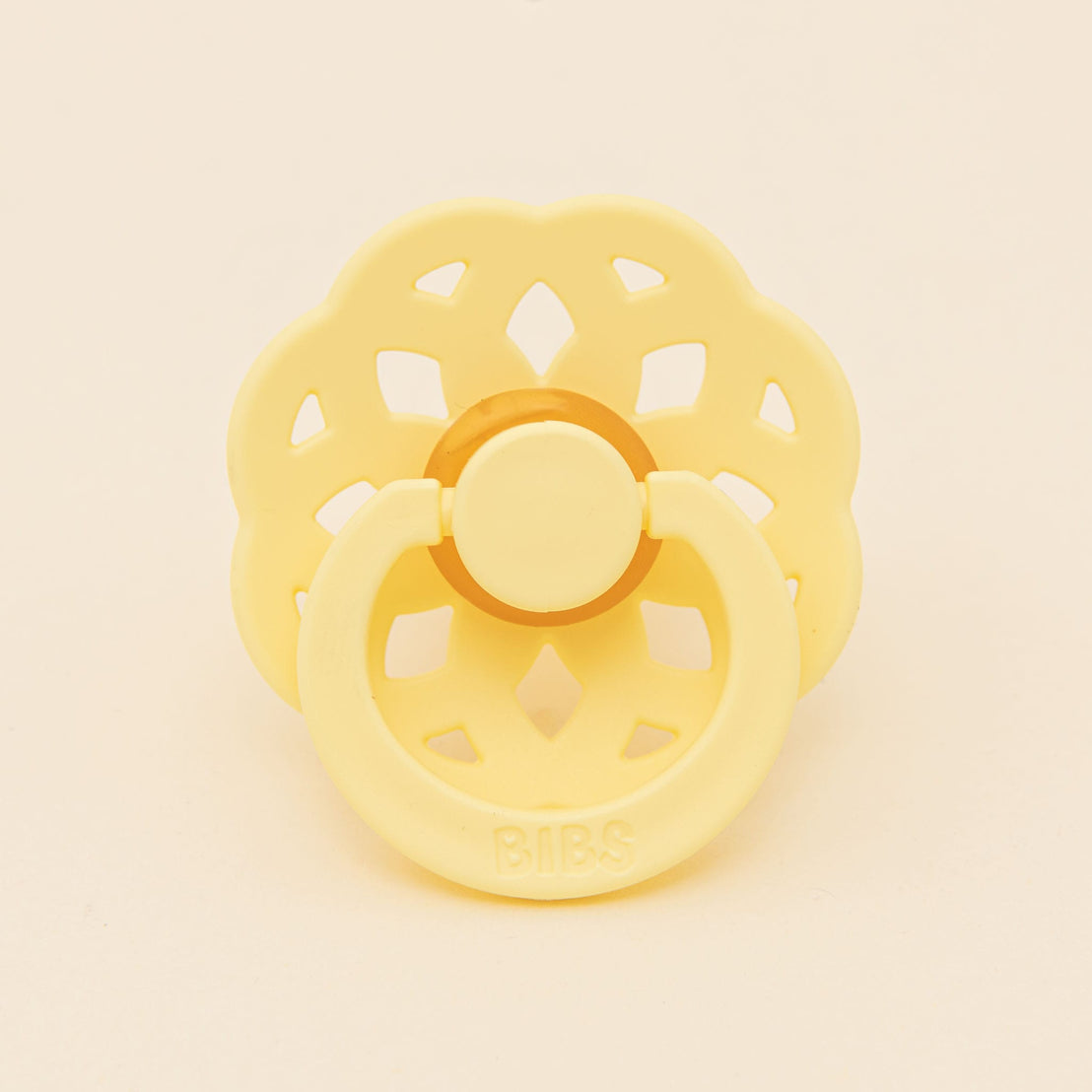 A yellow Bibs Lace pacifier with a flower-shaped shield and handle, set against a neutral background. The brand "bibs" is embossed on the front.