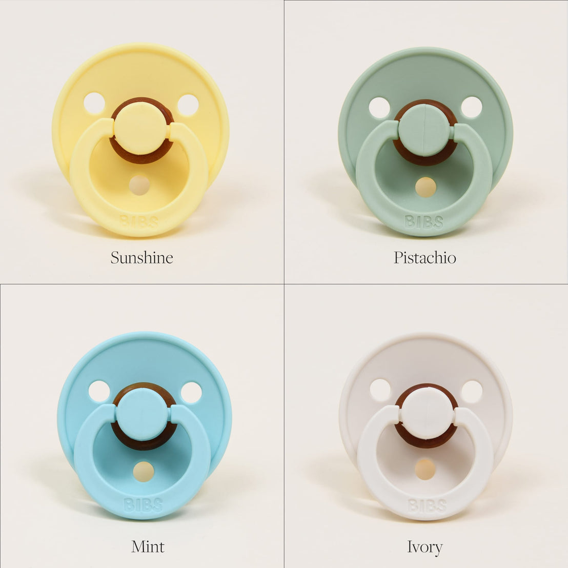 Four Bibs Pacifiers in different colors labeled as sunshine, pistachio, mint, and ivory, displayed against a plain background. Each pacifier has a distinctive round shield and button handle.