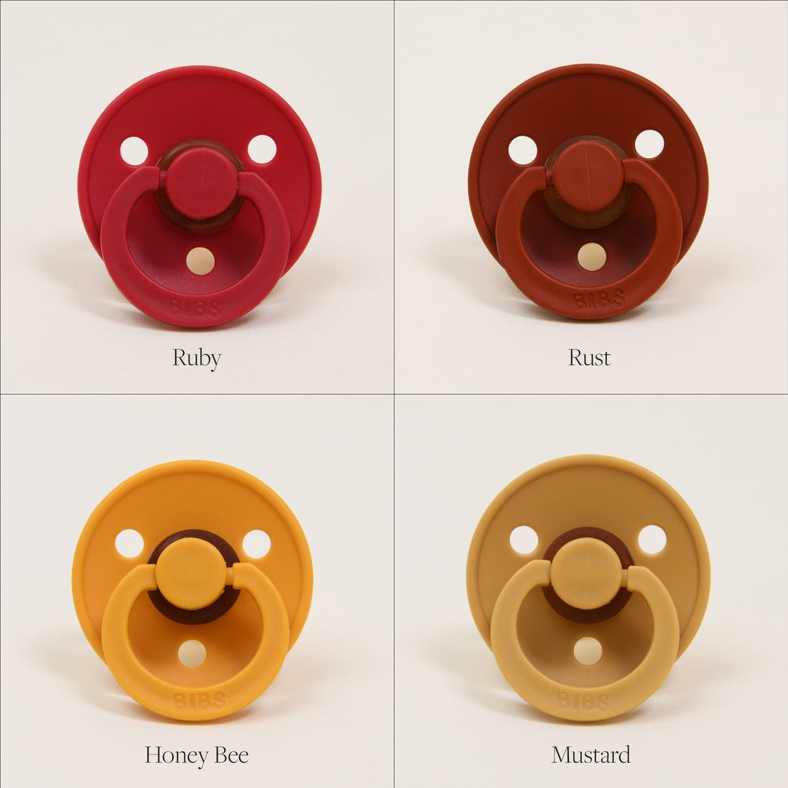 Four colorful Bibs Pacifiers against a white background, displayed in squares. Top left: ruby (red), top right: rust (brown), bottom left: honey bee (yellow), bottom right: