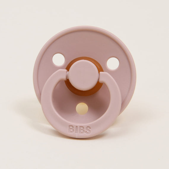 A Bibs Pacifier in Blush with a round shield and two ventilation holes, featuring a brown rubber nipple and a ring handle, set against a plain white background.