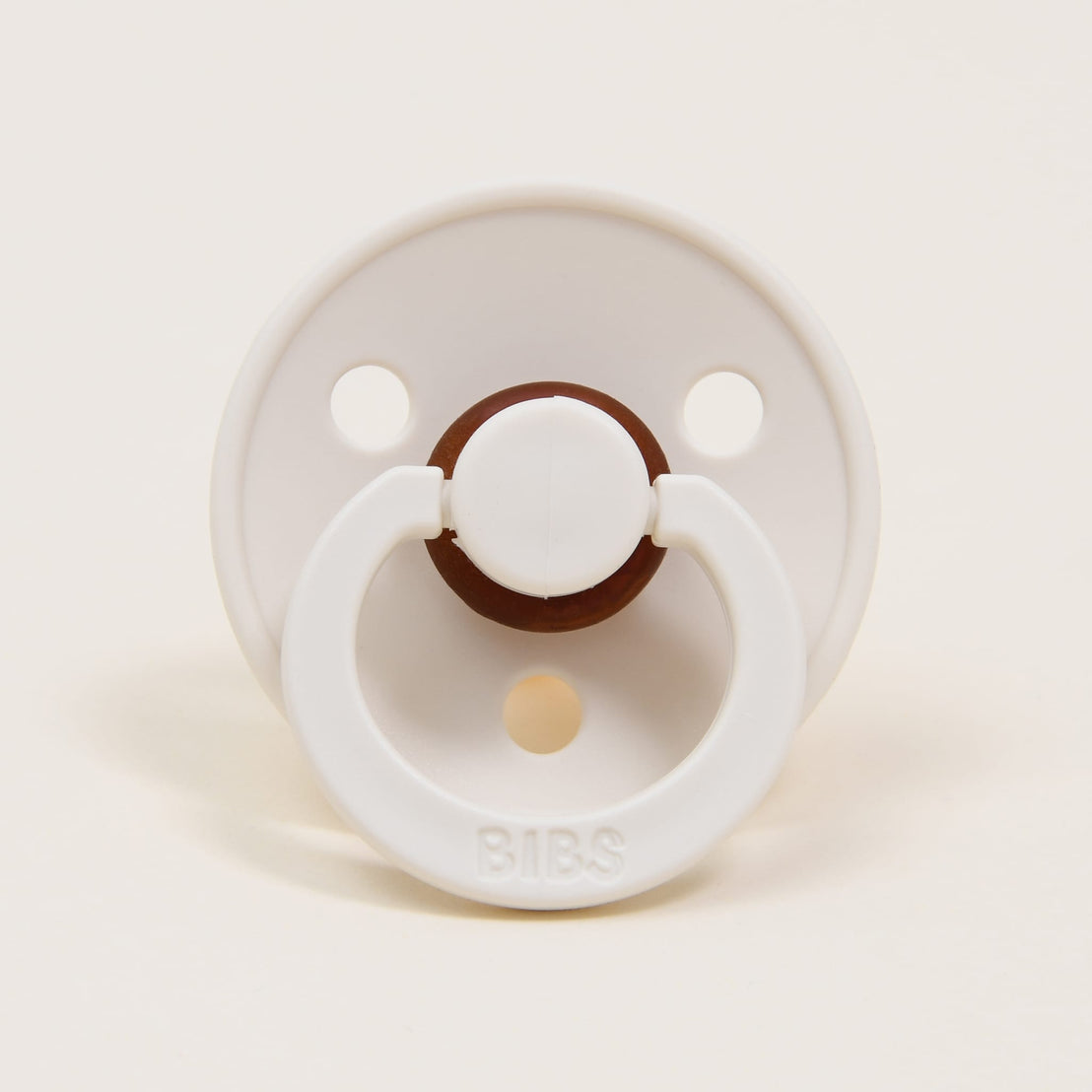 A Bibs Pacifier in Ivory with a brown center button and handle, set against a plain beige background.