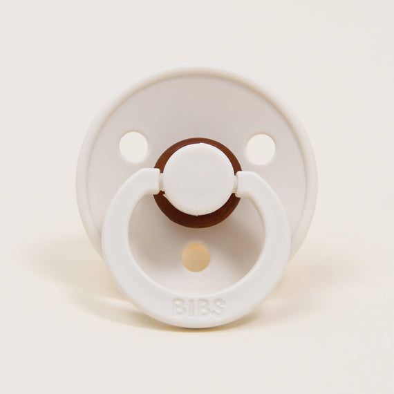 A Bibs Pacifier in Ivory with a brown center button and handle, set against a plain beige background.