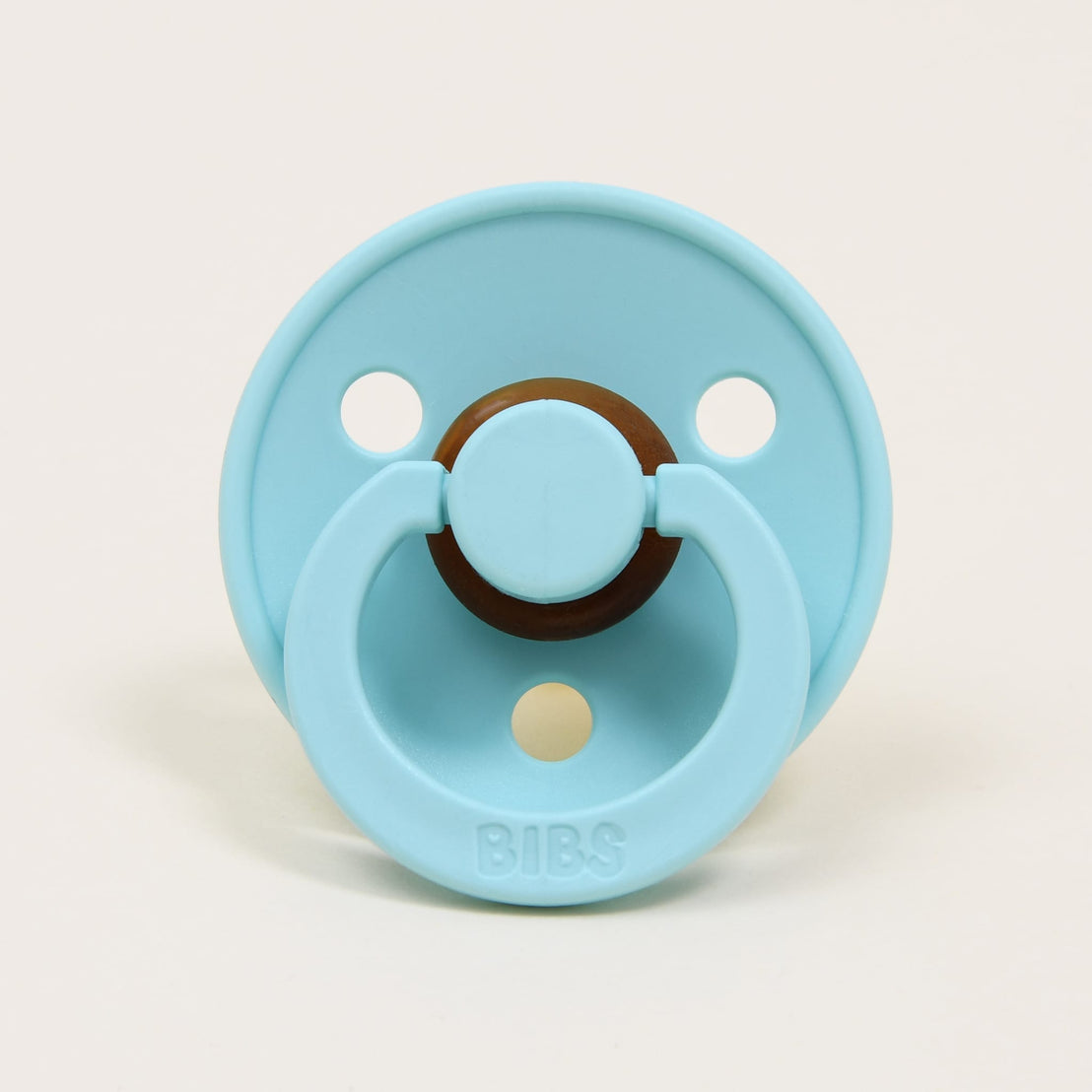 A mint green pacifier with a round brown handle and the brand name "bibs" written at the top, designed in Denmark, set against a plain white background.