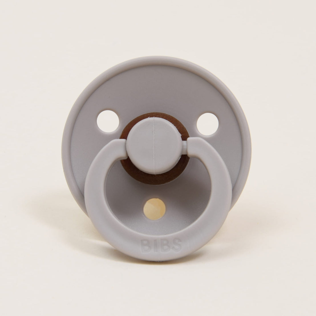 A Bibs Pacifier in Sand featuring an upscale design with two air holes and a natural brown button handle, set against a plain white background. Perfect as a baby gift.
