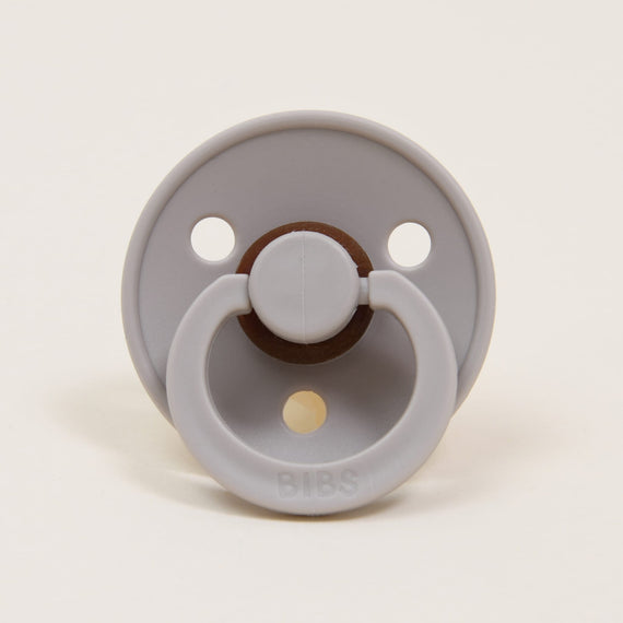 A Bibs Pacifier in Sand featuring an upscale design with two air holes and a natural brown button handle, set against a plain white background. Perfect as a baby gift.