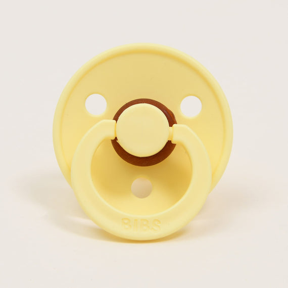 A yellow Bibs Pacifier in Sunshine color with a brown button detail, branded "bibs".