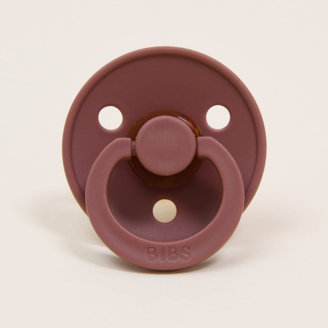 A maroon-colored Bibs Pacifier with three air holes, featuring a handle and "bibs" brand name on the button.