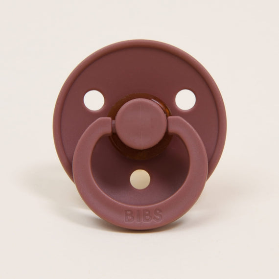 A maroon-colored Bibs Pacifier with three air holes, featuring a handle and "bibs" brand name on the button.