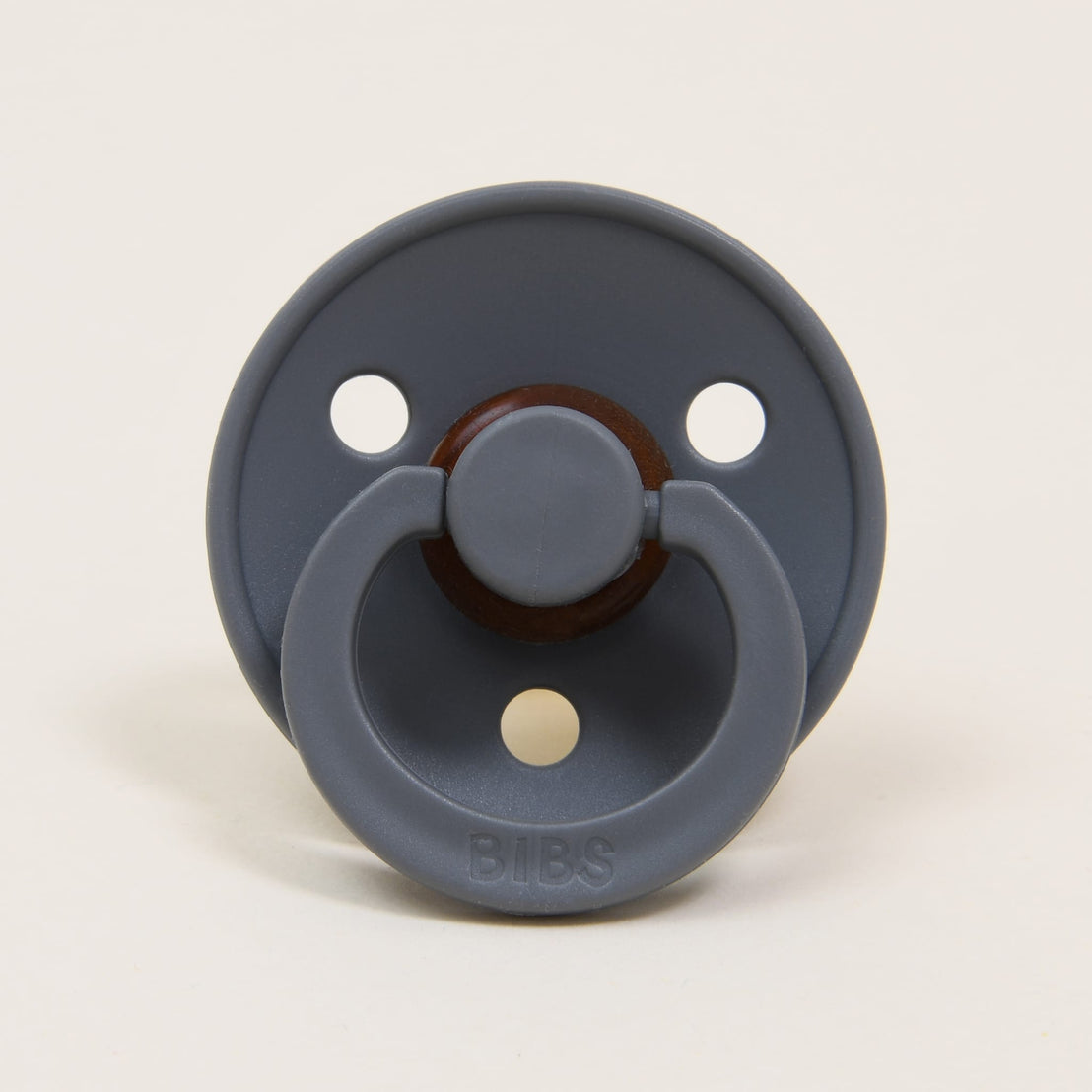 A dark grey Bibs Pacifier with a round natural nipple, and a ring-shaped plastic handle, marked with the brand name "bibs".