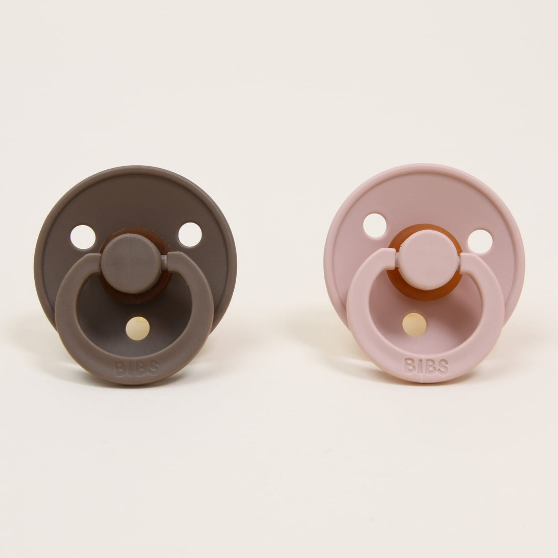 Two Bibs Pacifiers, one brown and one pink, displayed against a plain white background.