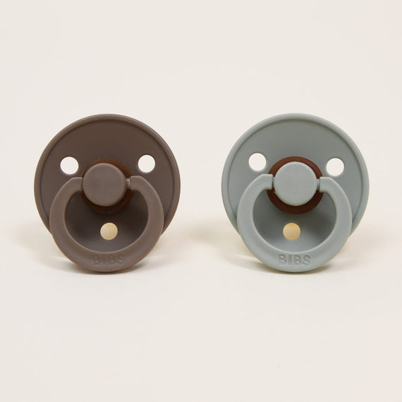 Two Bibs Pacifiers in "dark oak" and "sage" colors against a plain background.