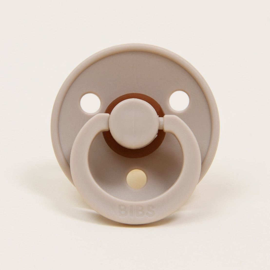 A bibs pacifier in the color vanilla, photographed against a beige backdrop.