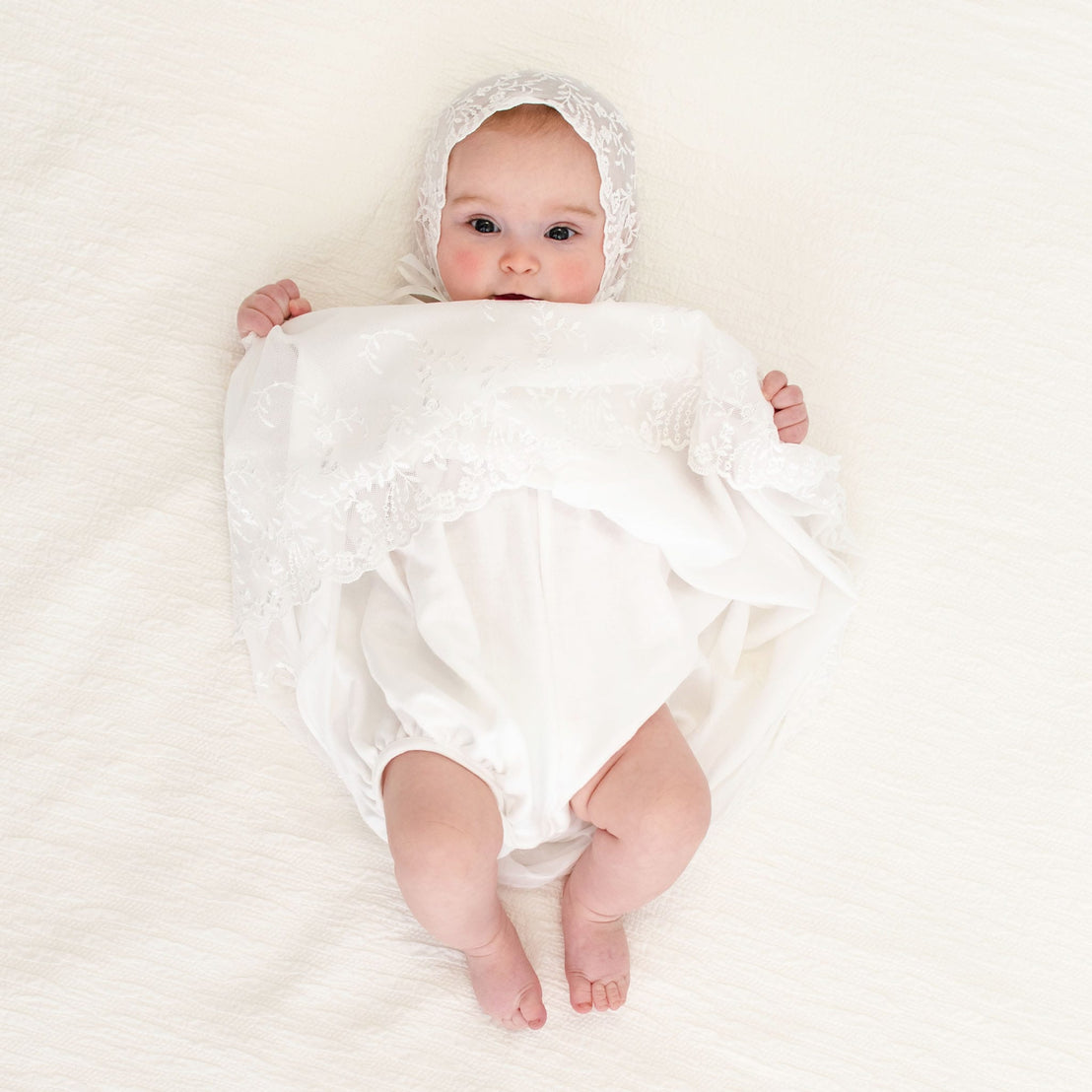 A baby girl holding up her skirt showcasing the undergarment of the Ella baptism dress.