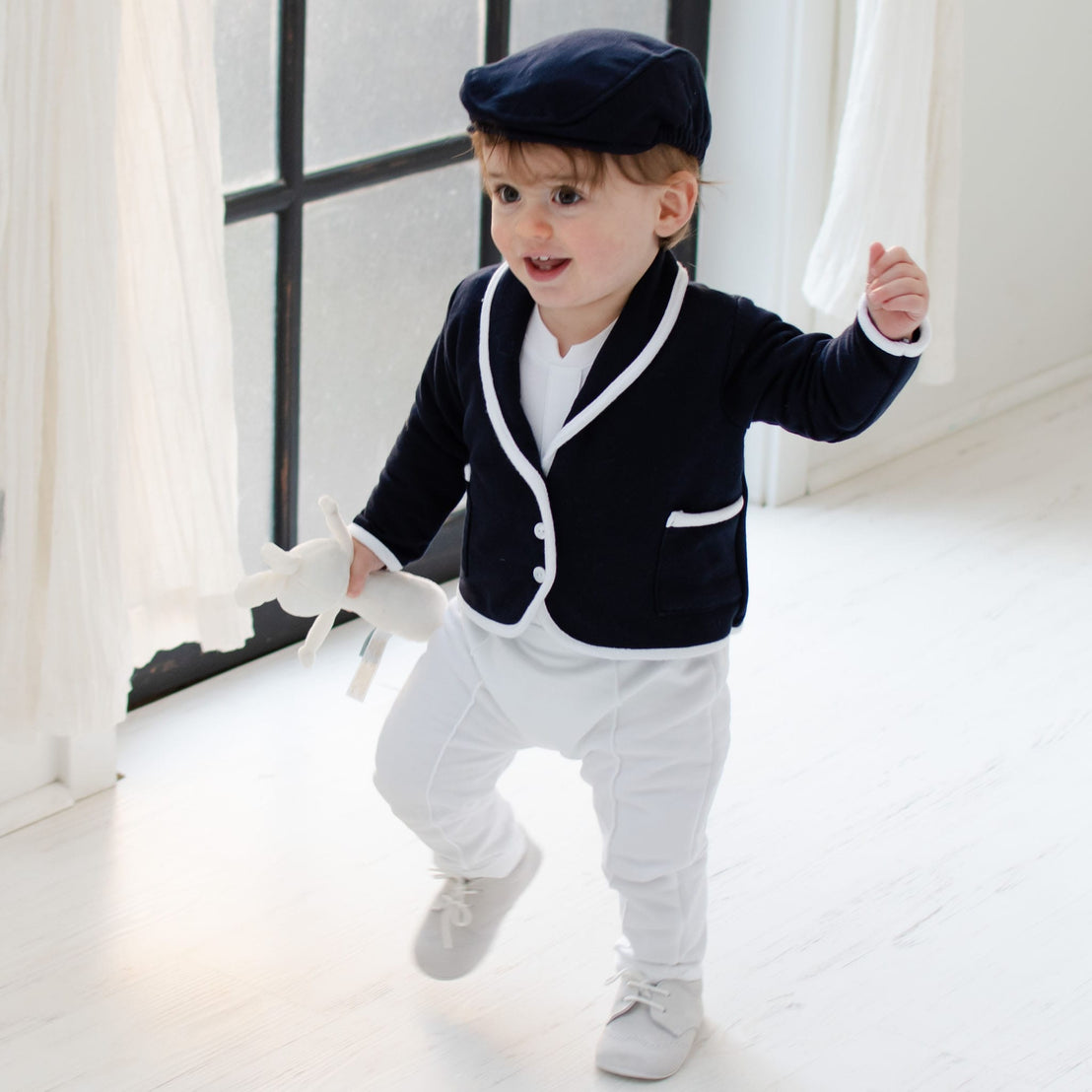 Smiling baby boy walking and wearing the Elliott 3-Piece Suit, including the jacket, pants, and onesie (and matching newsboy cap)