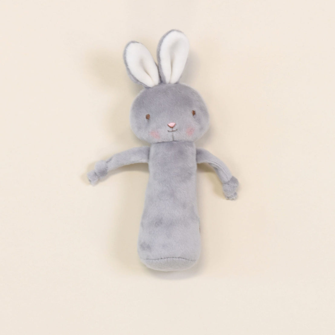 A soft and baby-safe Friendly Chime Rattle in gray, featuring velour chimes and long ears, is set against a light beige background. This plush toy boasts pink cheeks and a cylindrical body with delicately embroidered facial features, making it ideal for gentle play.