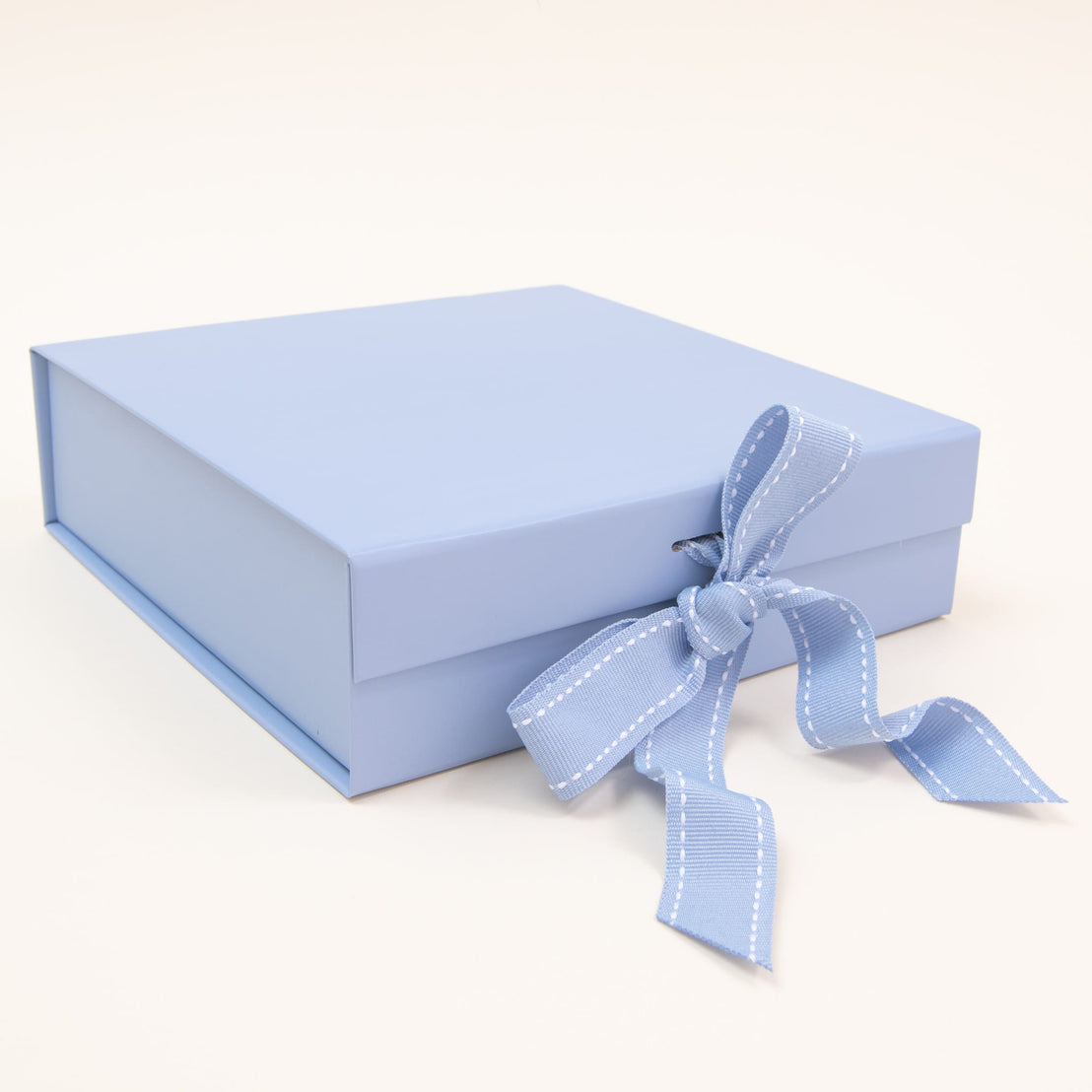 A pastel blue small gift box with a matching ribbon tied in a bow, exuding elegance, rests gracefully against a plain white background. This square-shaped box is by Baby Beau & Belle.