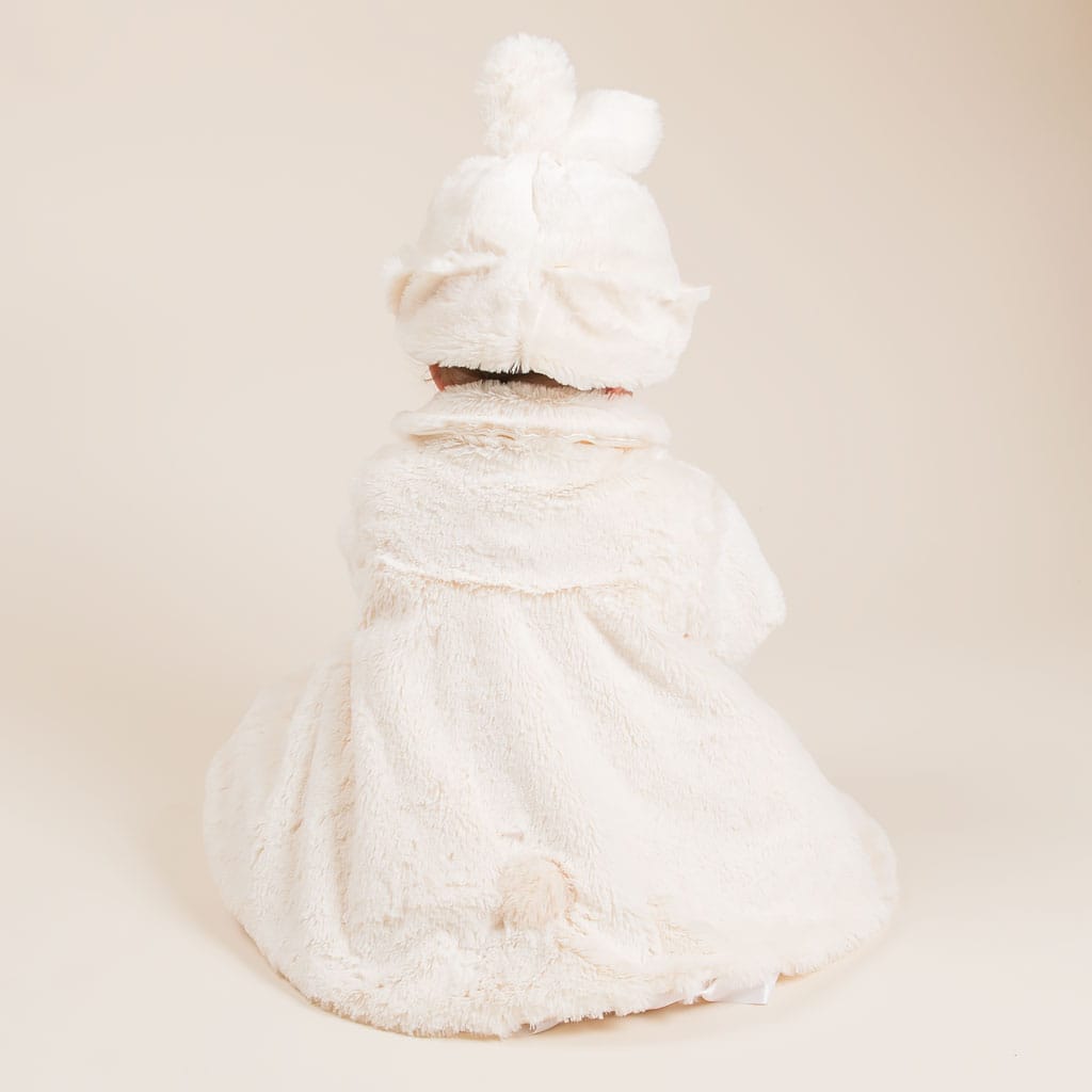 A baby dressed in the Glad Dreams Coat Set, featuring a fluffy white bear costume with ears and a pom-pom hat, sits facing away from the camera against a plain background—a truly unique baby gift.