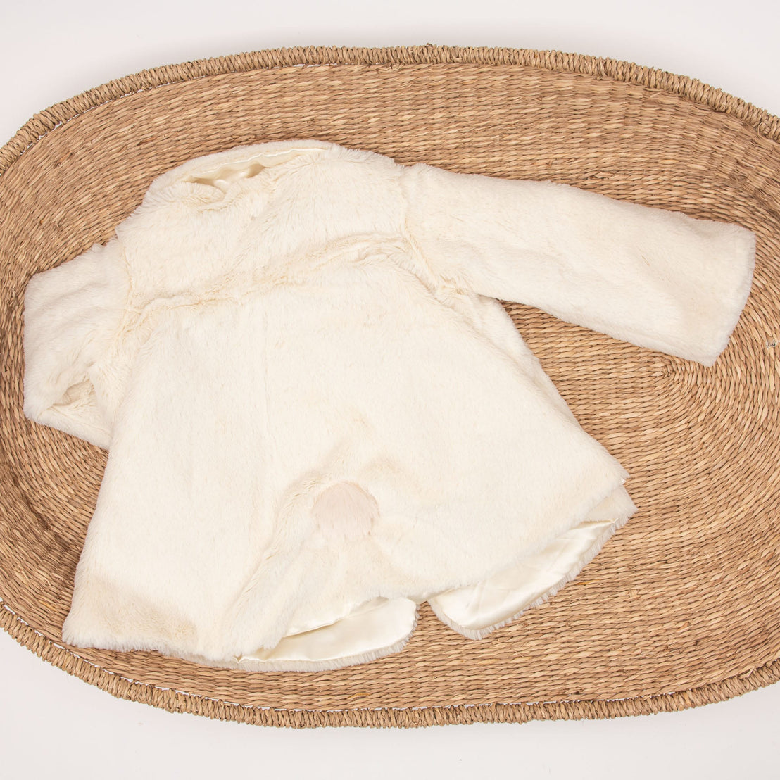 A unique baby gift, the Glad Dreams Coat Set in pristine white features long sleeves and is elegantly displayed on an oval woven rattan mat. The back of the coat faces up, revealing a lightly stained area near the bottom that adds a touch of character to this charming winter essential.