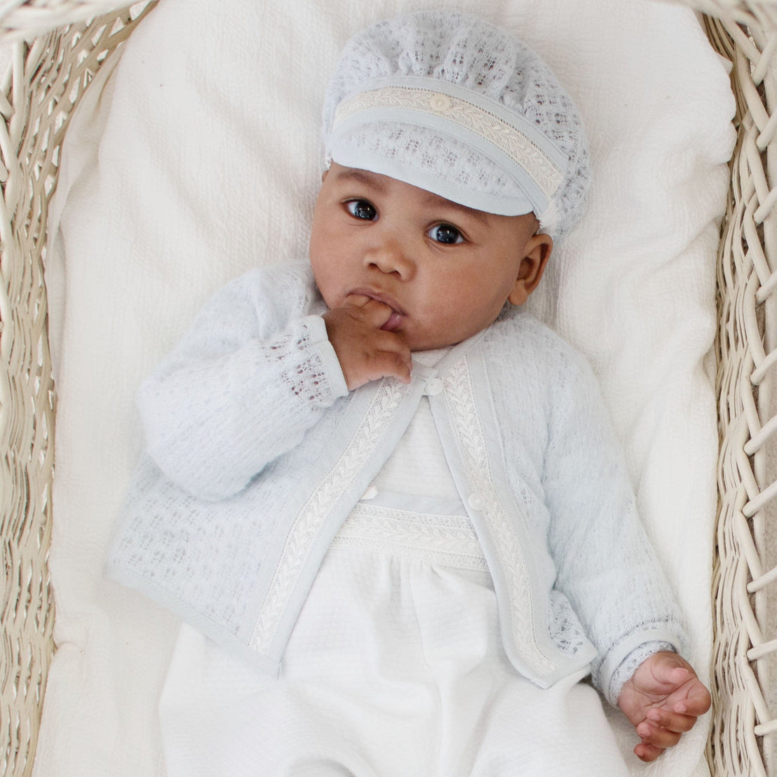 Baby lying in a wicker cradle, wearing a soft blue knit sweater with lace details, paired with a white long-sleeve romper.