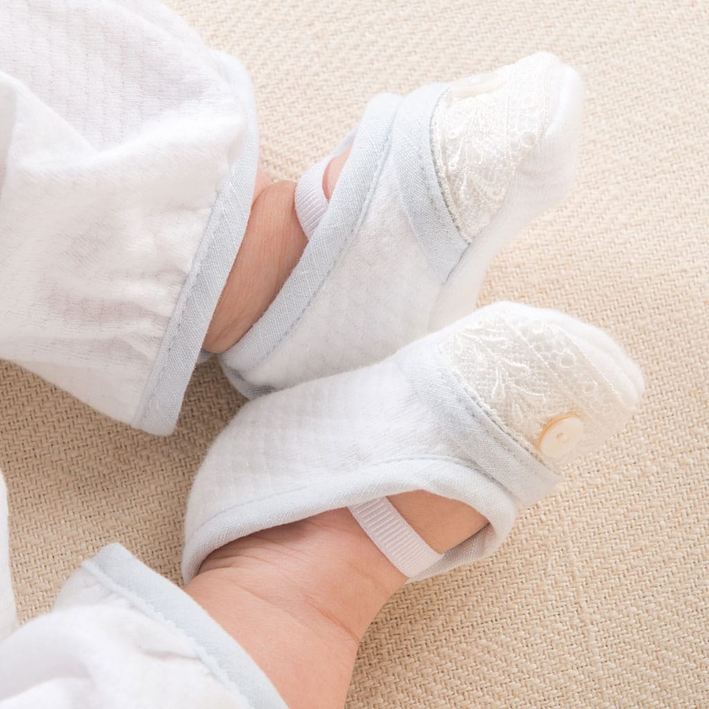 A baby’s feet wearing the Harrison quilted booties, featuring lace detailing and a button accent.