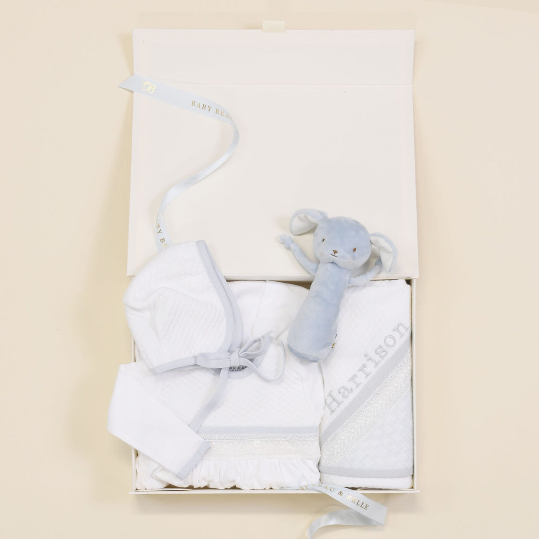 The Harrison Newborn Gift Set box showing the gown, plush bunny rattle, personalized blanket, and hat, elegantly presented with a Baby Beau & Belle ribbon.