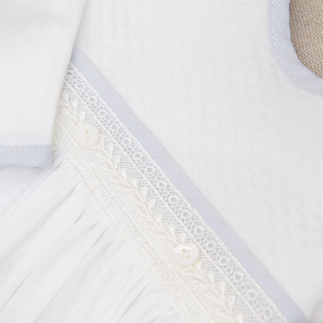 A detailed close-up of the lace waistband on the Harrison Newborn Gown, showcasing the textured fabric and delicate white buttons.