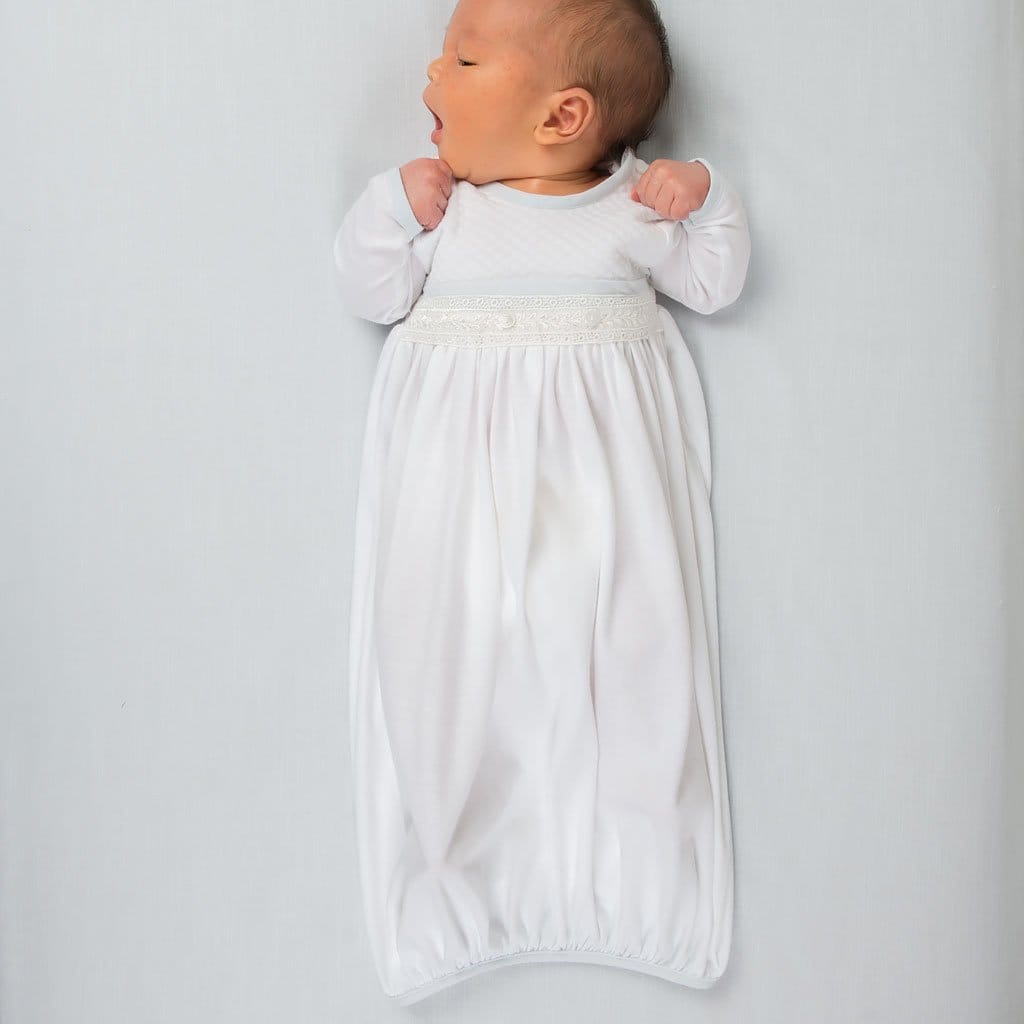 A newborn baby yawning while lying on a soft surface, dressed in the Harrison Newborn Gown with a flowing silhouette and lace trim for a cozy fit.