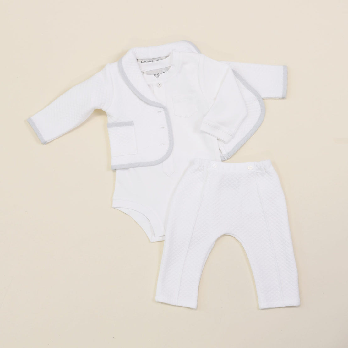 The Harrison Quilted Newborn Suit laid flat, displaying the matching quilted jacket, bodysuit, and pants in soft white fabric with blue trim.