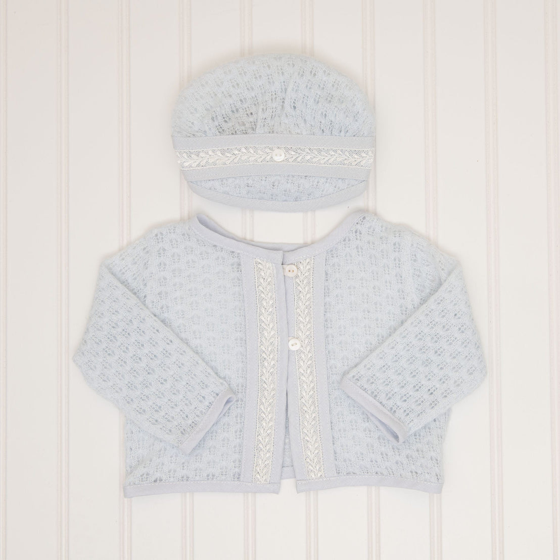 A flat lay of the Harrison Blue Knit Sweater and Blue Knit Hat, showcasing the fine lace trim and pearl-like buttons on the front.